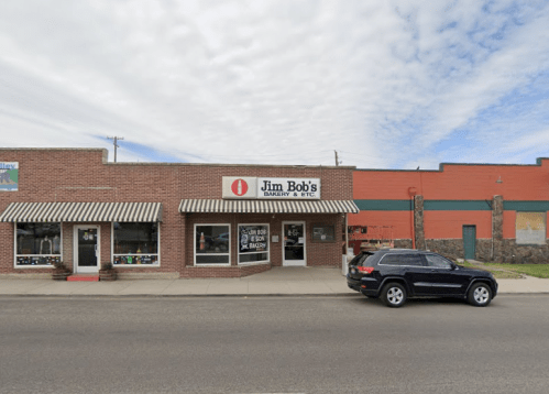 A brick building with a striped awning, featuring "Jim Bob's Bakery & Etc." sign, parked SUV in front.