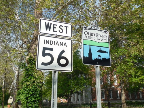 Signpost indicating West Indiana 56 and Ohio River Scenic Byway, surrounded by trees and greenery.