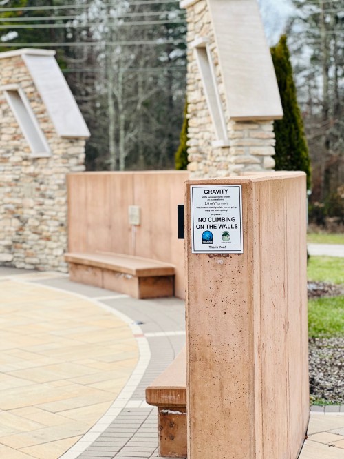Sign on a stone wall warns, "No climbing on the walls," in a landscaped outdoor area.
