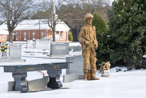 A soldier statue stands in a snowy cemetery, surrounded by gravestones and a bench marked "Emma" and "Pete."