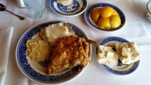 A plate of fried chicken with gravy, corn, biscuits with butter, and a side of peaches on a blue-patterned dish.
