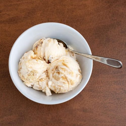 A bowl of three scoops of ice cream with a spoon, resting on a wooden surface.