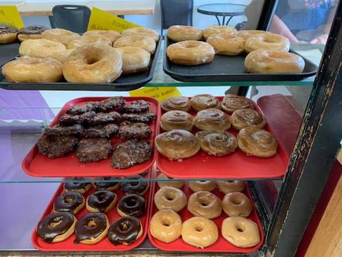 A display case with trays of assorted donuts, including glazed, chocolate-covered, and cinnamon rolls.