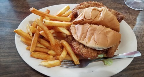 A plate with two fried chicken sandwiches on buns, lettuce, and a side of golden French fries.