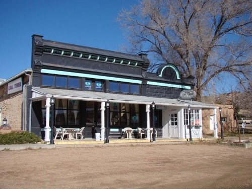 Historic building with a black facade, turquoise accents, and outdoor seating under a clear blue sky.