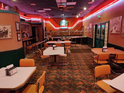A retro diner interior with empty tables, orange chairs, and neon lights along the walls.
