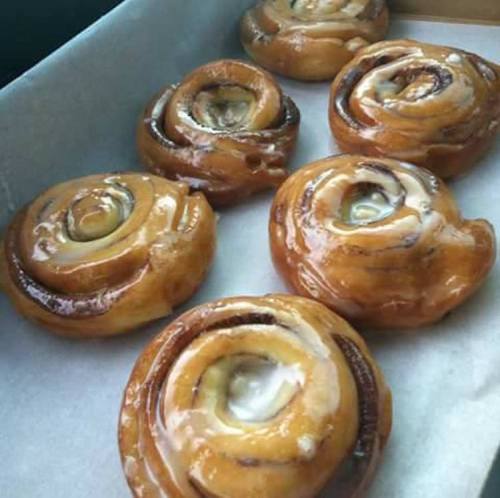 A tray of freshly baked cinnamon rolls with a glossy glaze, arranged neatly on parchment paper.