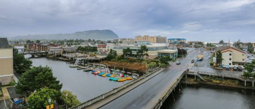 A coastal town with colorful kayaks on a river, surrounded by buildings and a misty mountain backdrop.