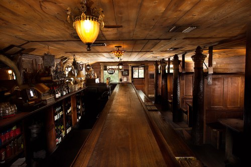 A rustic bar interior with wooden beams, a long counter, and warm lighting, creating a cozy atmosphere.
