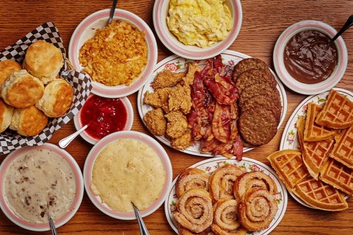 A spread of Southern breakfast foods including biscuits, fried chicken, bacon, waffles, grits, and cinnamon rolls.