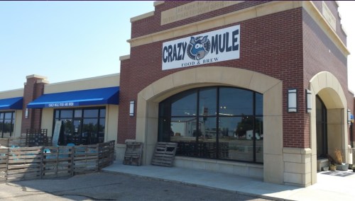 Exterior of Crazy Mule Food & Brew, featuring a large sign and windows, with a brick facade and blue awnings.