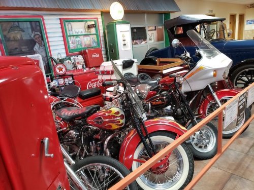 A collection of vintage motorcycles and classic cars displayed in a museum setting, featuring bright colors and retro decor.