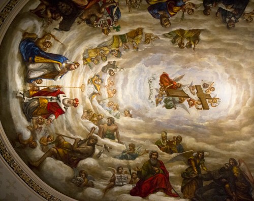 A detailed fresco depicting various figures in clouds, with a central figure holding a cross and surrounded by angels and saints.