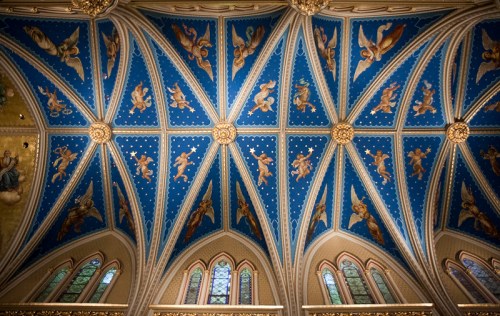 Ornate blue ceiling with gold accents and angelic figures, featuring intricate patterns and stained glass windows below.