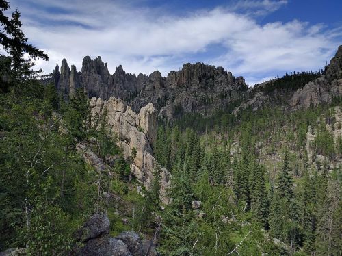 A scenic view of rugged mountains and dense green forests under a partly cloudy sky.