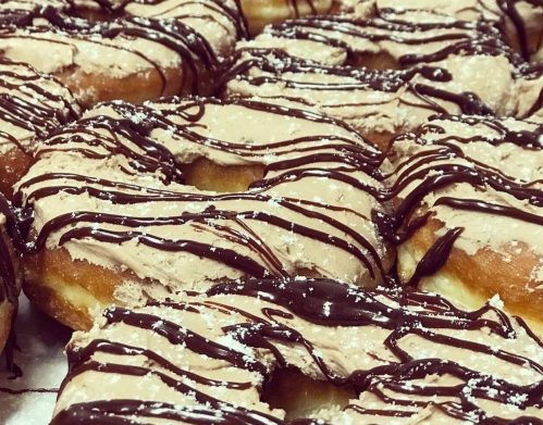 A close-up of freshly glazed donuts drizzled with chocolate and topped with a light frosting.