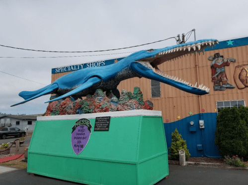 A large blue whale statue with an open mouth, set on a colorful base outside a specialty shop.