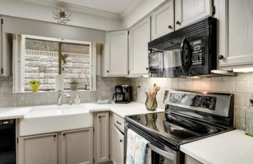 A modern kitchen with light cabinets, a black microwave, and a window overlooking a garden.