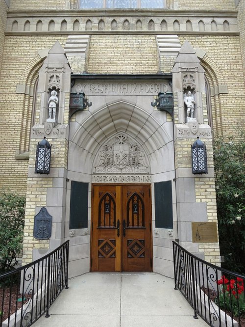 Entrance of a historic building featuring ornate stonework, wooden double doors, and decorative sculptures.