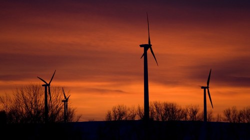 Silhouetted wind turbines against a vibrant sunset sky with orange and purple hues.