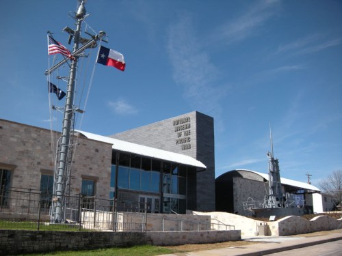 Exterior view of the Museum of the Pacific War, featuring flags and modern architecture against a clear blue sky.