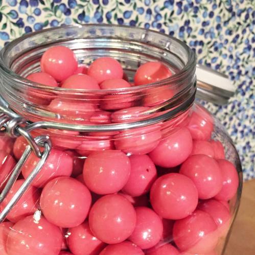 A glass jar filled with bright pink round candies against a floral-patterned background.