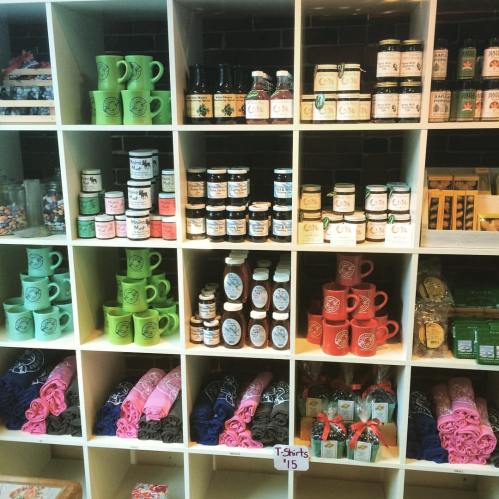 A display shelf filled with colorful mugs, jars, and T-shirts in a variety of colors and designs.