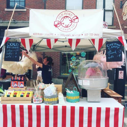 A colorful candy stand with cotton candy and drinks, set up in a bustling street market.