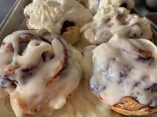 Freshly baked cinnamon rolls topped with creamy icing, arranged on a baking tray.