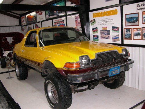 A vintage yellow and maroon car with oversized tires displayed in a museum setting.
