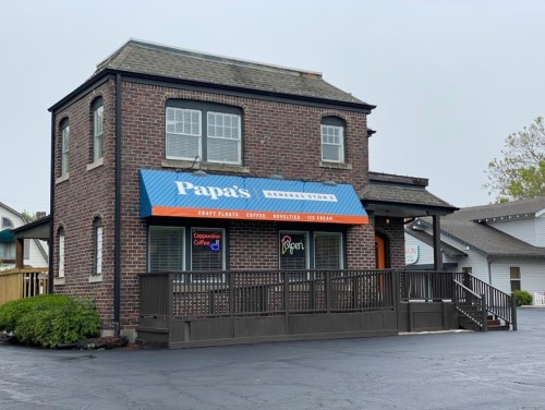A brick building with a blue awning reading "Papa's General Store," featuring a porch and parking area.