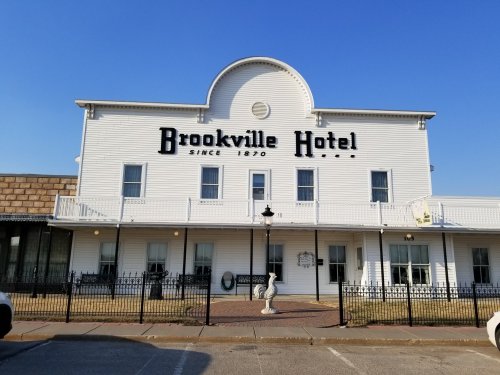 Exterior of the Brookville Hotel, a historic building with white siding and a sign, under a clear blue sky.