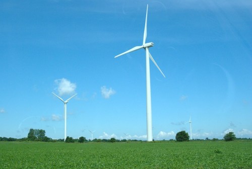 A landscape featuring several tall wind turbines against a clear blue sky and green fields.