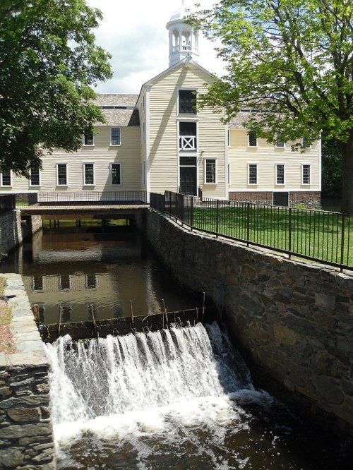 Historic building with a cupola, overlooking a stone wall and a small waterfall, surrounded by greenery.