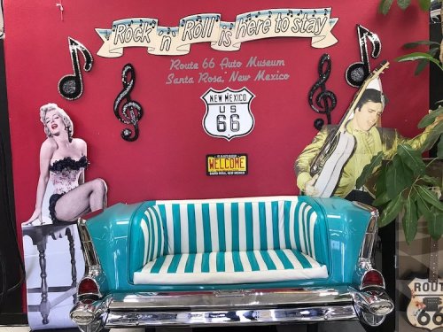 A retro turquoise couch in front of a red wall with music notes, featuring cutouts of Marilyn Monroe and Elvis Presley.