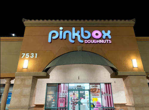Exterior of Pinkbox Doughnuts store at night, featuring a colorful sign and open storefront.