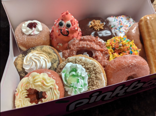 A colorful assortment of donuts in a pink box, featuring various toppings and decorations.
