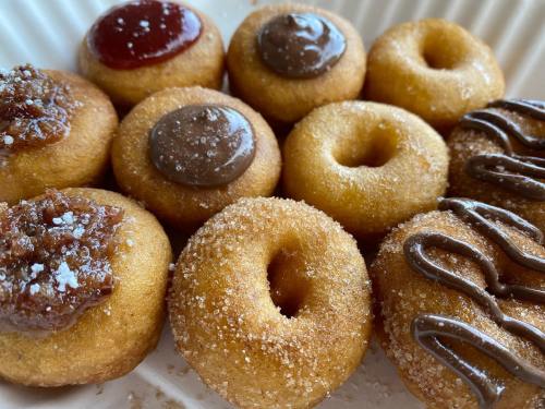 A close-up of mini donuts topped with chocolate, strawberry, and cinnamon sugar, arranged on a white plate.