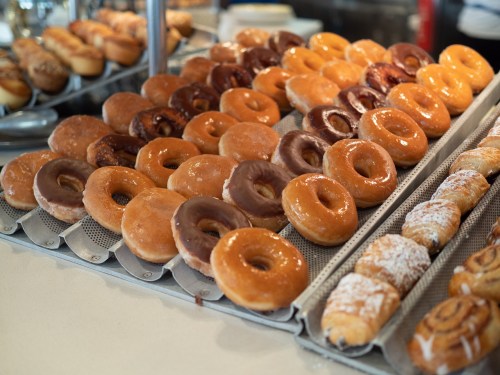 A variety of glazed and chocolate-covered donuts arranged on display trays in a bakery.
