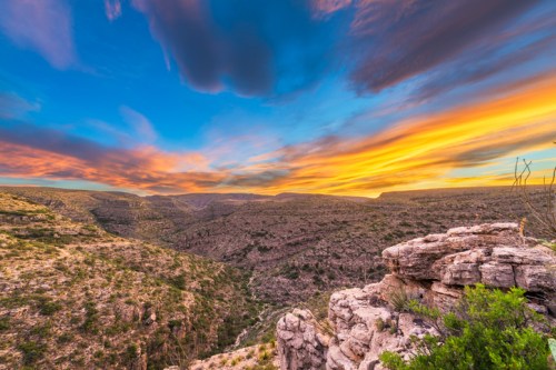 Vibrant sunset over a rugged canyon landscape, with colorful clouds and rocky terrain in the foreground.