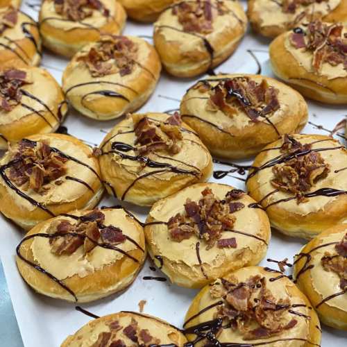 A tray of donuts topped with peanut butter frosting, crispy bacon bits, and drizzled with chocolate.