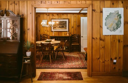 Cozy wooden dining area with a table, chairs, and a vintage chandelier, framed by a rustic wooden archway.