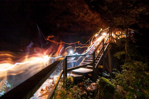 A wooden staircase illuminated by swirling lights, surrounded by dark trees at night.