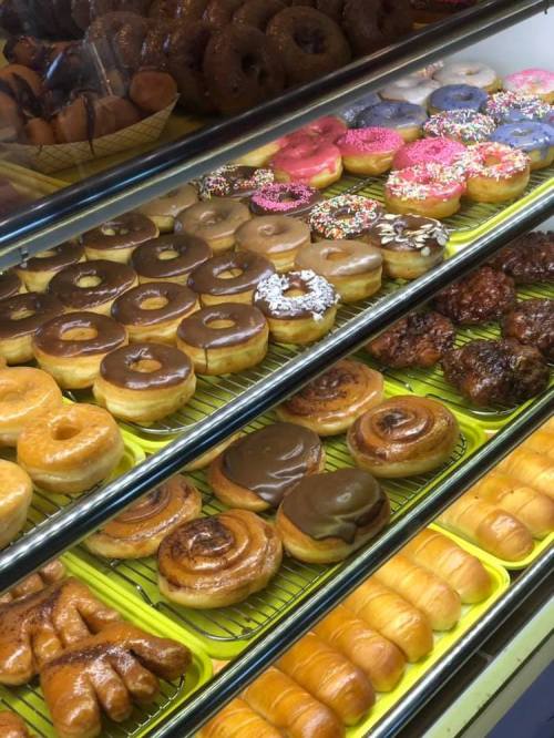 A display case filled with various colorful donuts, including glazed, chocolate, and sprinkled varieties.