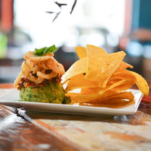 A plate of guacamole topped with crispy onions, served with a side of tortilla chips on a wooden table.
