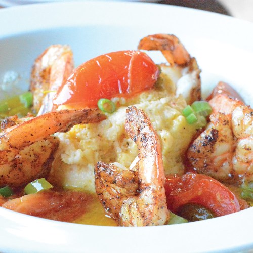 A close-up of a dish featuring grilled shrimp, tomatoes, and a creamy base, garnished with green onions.