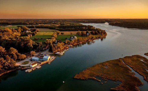 Aerial view of a serene river landscape at sunset, featuring lush greenery and a small dock.