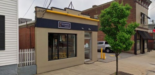 Exterior view of a small restaurant with a yellow awning, large windows, and a tree in front.