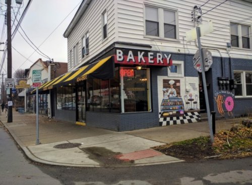 A cozy bakery with an "Open" sign, featuring a striped awning and colorful donut mural on the side.