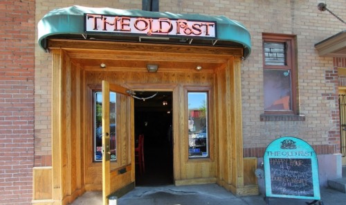 Entrance of "The Oldest" restaurant with wooden doors and a chalkboard sign advertising happy hour and burger night.
